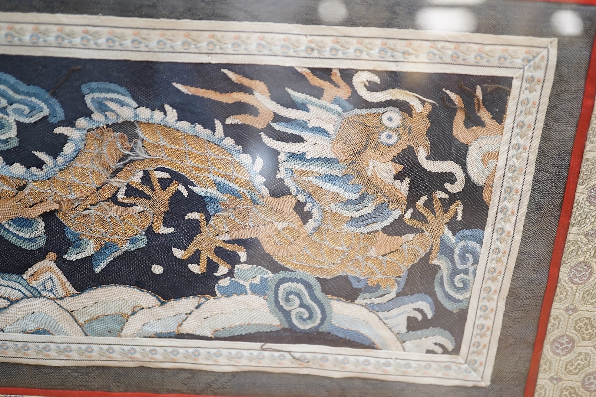 A Chinese framed Kesi gold dragon embroidery, probably originally part of a robe, together with a Chinese framed silk embroidered butterfly sleeve band, both items edged with narrow silk braiding and bordered with silk b